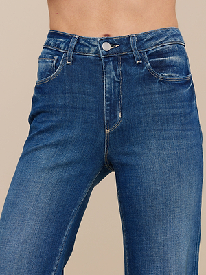 A close-up of a person wearing the Scottie Wide-Leg Jean, featuring a high-rise vintage wash, front pockets, belt loops, and a button closure. The wide-leg silhouette stands out against a plain neutral background.