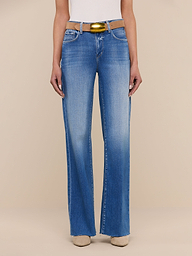 A person wearing the Scottie Wide-Leg Jean in light blue with a raw hem, paired with a white top, a yellow belt, and beige shoes stands against a plain white background.