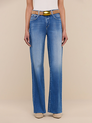 Wearing the Scottie Wide-Leg Jean in light blue with a raw hem and front fading, styled with a brown belt and beige shoes, this person stands against a plain beige background.