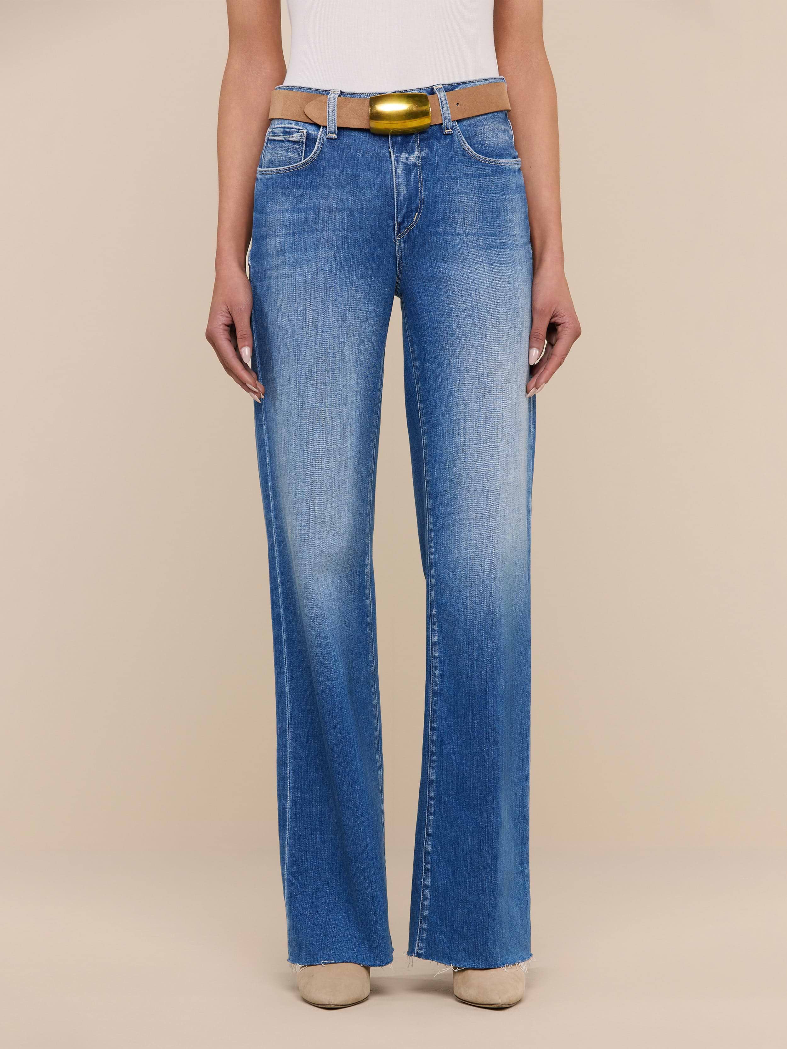 A person wearing the Scottie Wide-Leg Jean in light blue with a raw hem, paired with a white top, a yellow belt, and beige shoes stands against a plain white background.