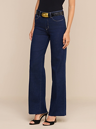 베이지색 배경 앞에 한 여성이 서 있는데, 스코티 와이드 레그 진을 입고 검은색 벨트와 검은색 오픈토 힐을 매치했다.