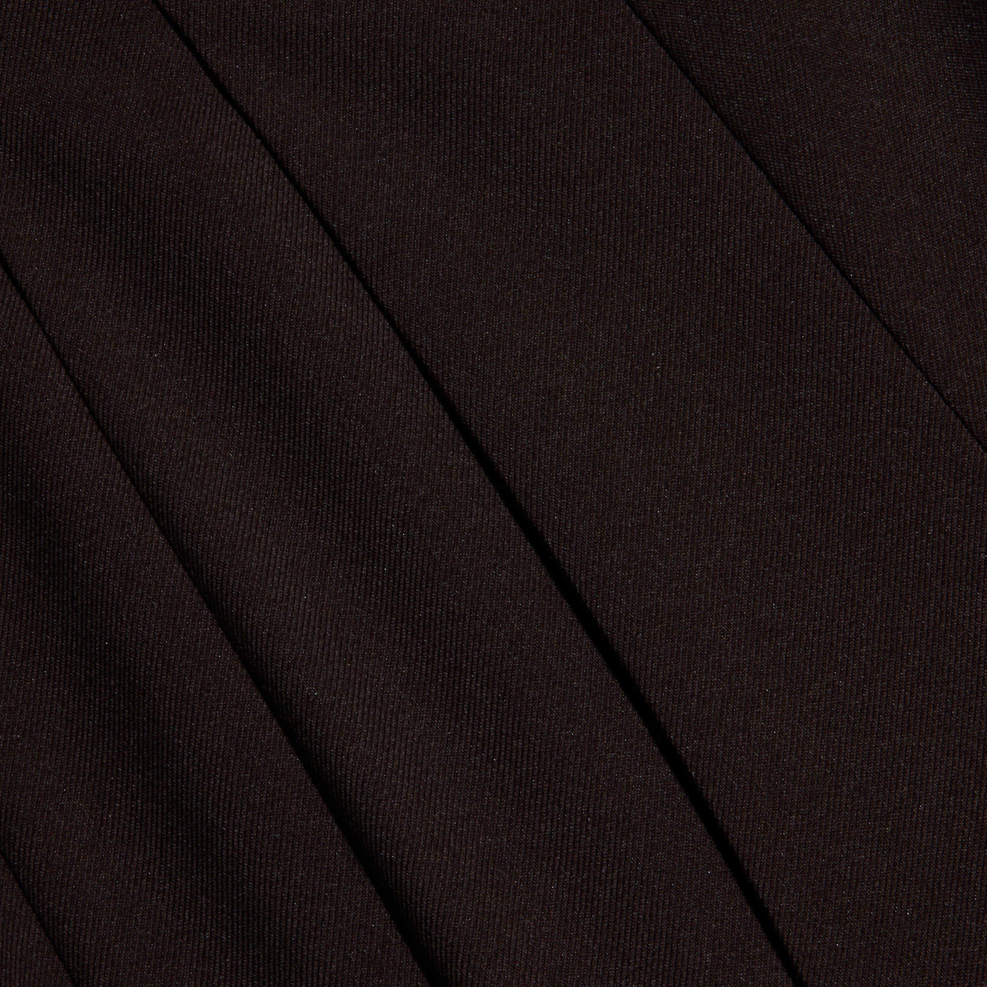 Close-up of black twill fabric with visible diagonal ribbing and seams, suggesting tailored clothing such as trousers or a skirt. The texture and folds create subtle shadows.