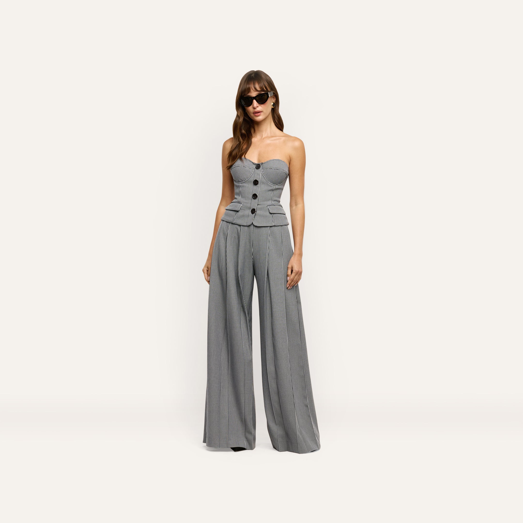 A person wearing a strapless, button-front bodice and Nova Pleated Wide-Leg Pant in a black-and-white houndstooth print.