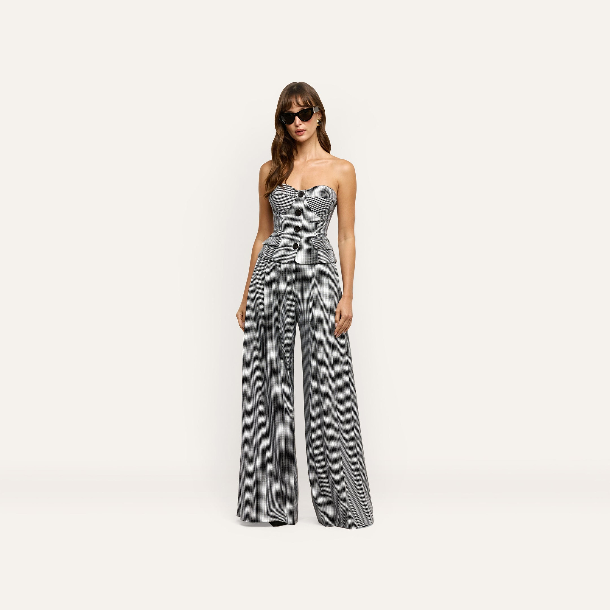 A person wearing a strapless, button-front bodice and Nova Pleated Wide-Leg Pant in a black-and-white houndstooth print.
