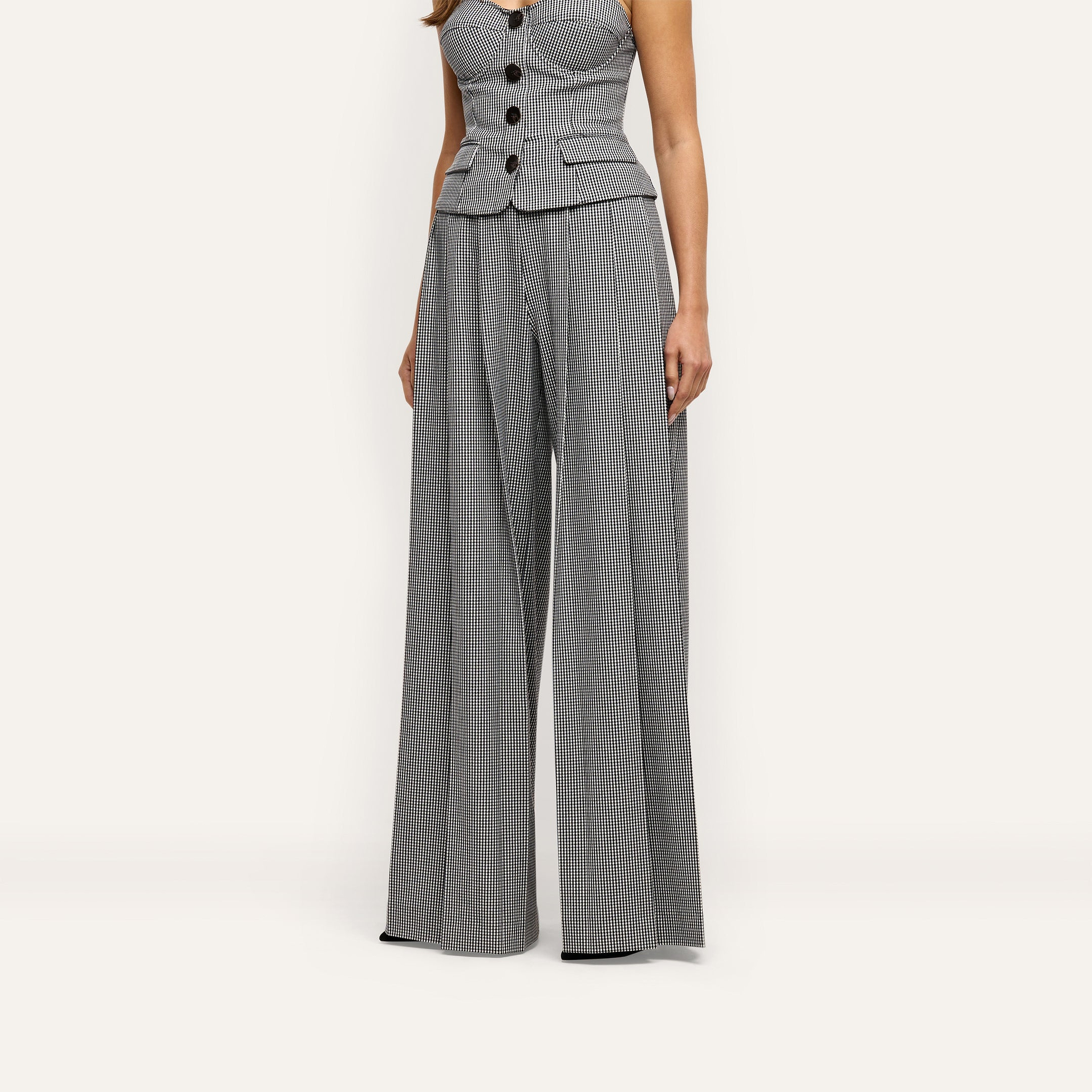 A person wearing a button-front peplum top and matching Nova Pleated Wide-Leg Pant in a black and white gingham suiting fabric.
