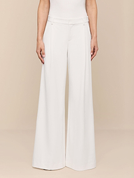 A person stands against a plain white background, shown from the shoulders down, wearing the Allanah Trouser—high-waisted, wide-leg trousers in white stretch suit fabric—paired with a sleeveless white top.