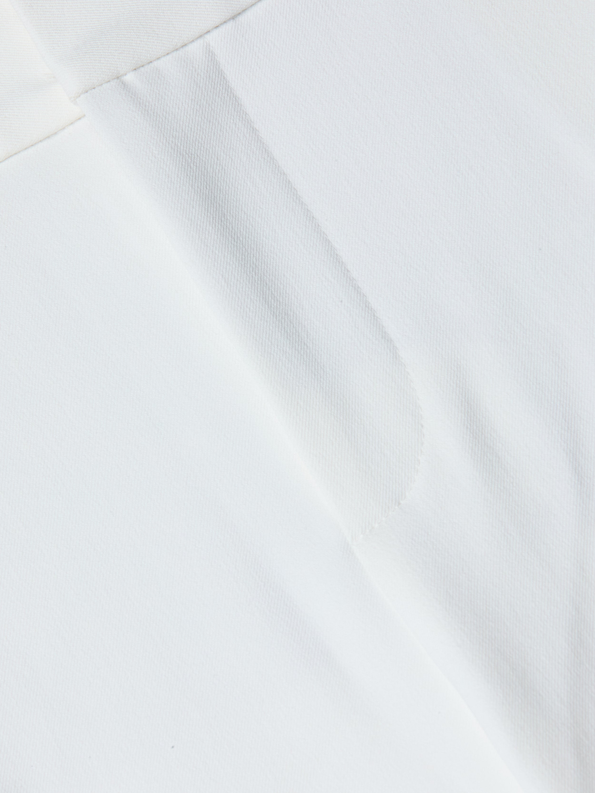 Close-up of the Allanah Trouser in white stretch fabric, featuring a visible seam and subtle texture that highlight its modern design details.