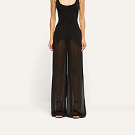 A person wearing a black bodysuit and Allanah Sheer Trouser, featuring mid-rise, sheer chiffon fabric with a floor-length, wide-leg silhouette.