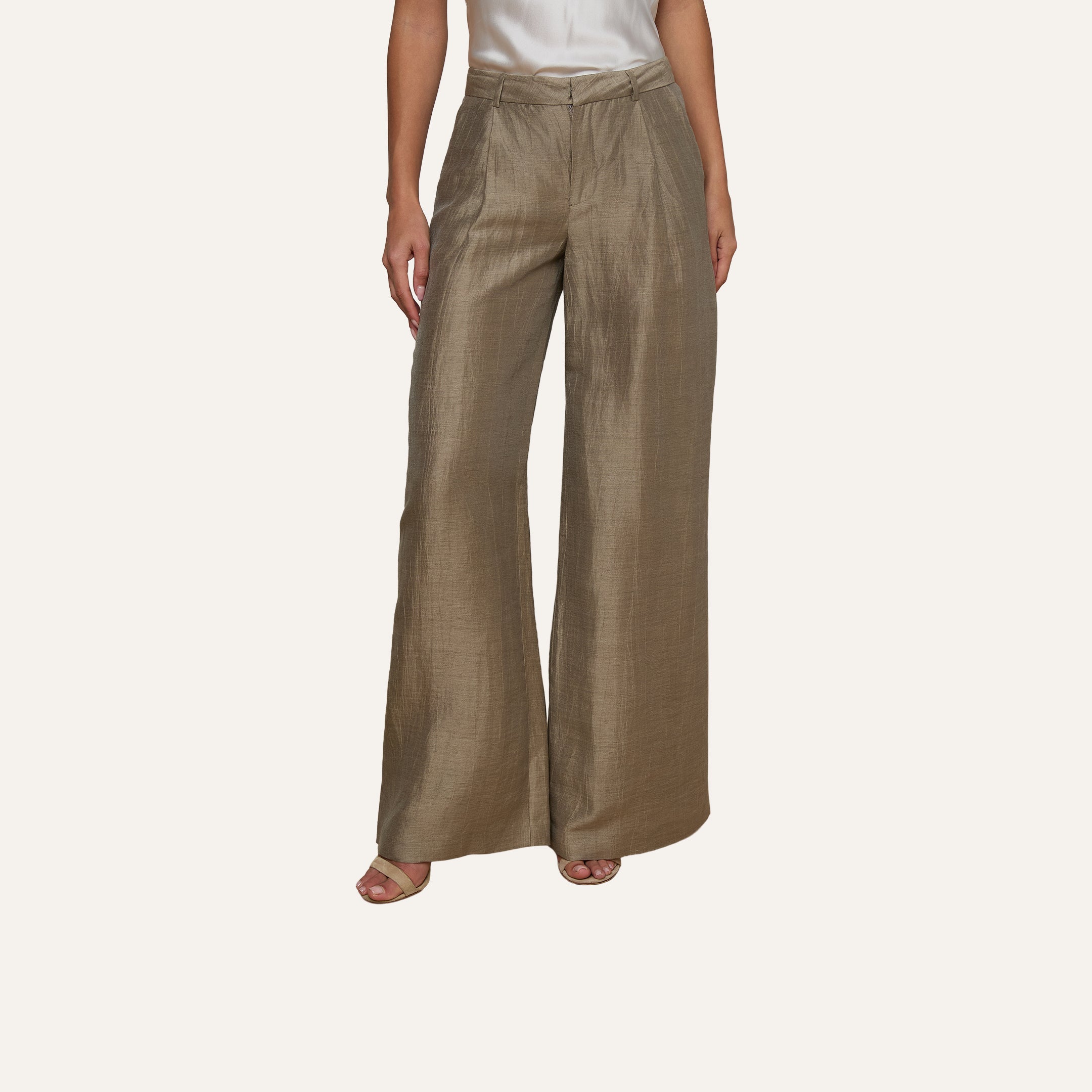 Wearing the Allanah Linen-Blend Trouser in light brown with a white sleeveless top, a person stands on a light wooden floor, only their lower half visible.