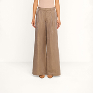 A person is shown from the shoulders down against a plain white background, wearing the Allanah Linen-Blend Trouser—high-waisted, wide-leg pants in latte brown with front pleats—paired with nude heels.