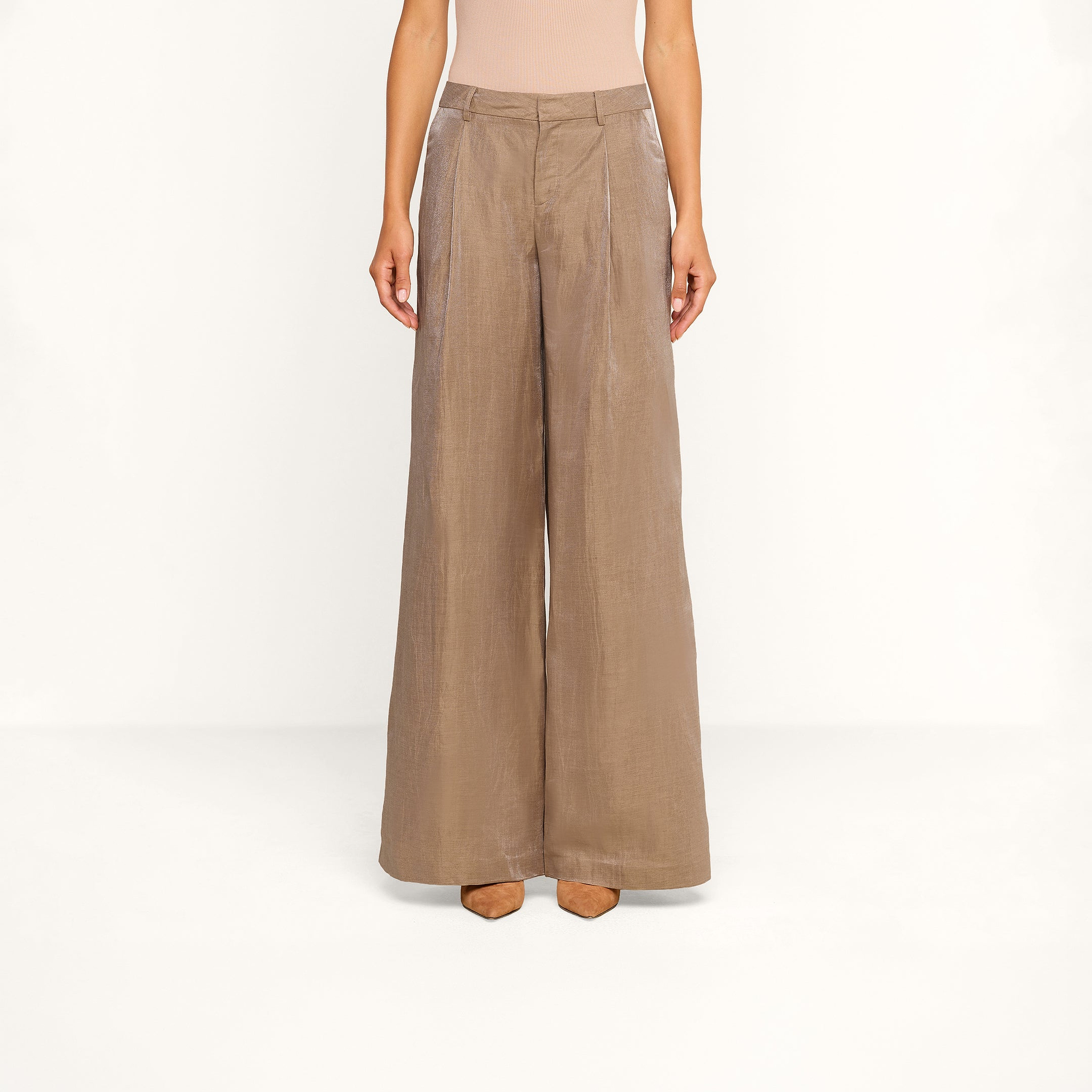 A person is shown from the shoulders down against a plain white background, wearing the Allanah Linen-Blend Trouser—high-waisted, wide-leg pants in latte brown with front pleats—paired with nude heels.