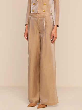 A person wearing shiny taupe wide-leg, modern Allanah Linen-Blend Trousers paired with a cropped jacket featuring gold buttons and pointed-toe heels. The ensemble is complemented by latte brown tones and the soft texture of the linen-blend pants.
