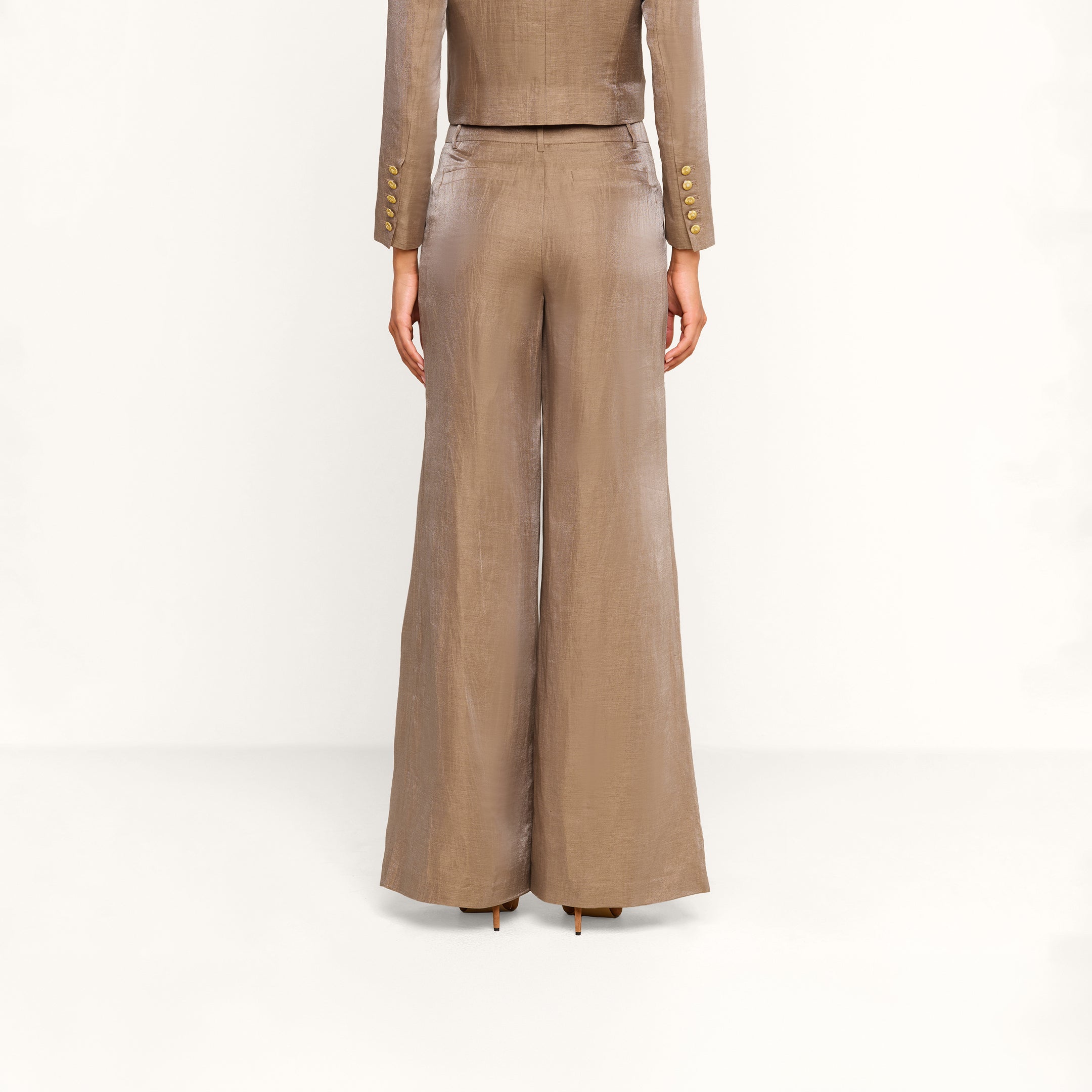 A person stands facing away, wearing a taupe-colored, tailored suit featuring the Allanah Linen-Blend Trouser with wide-leg styling and a matching blazer, set against a plain white background.
