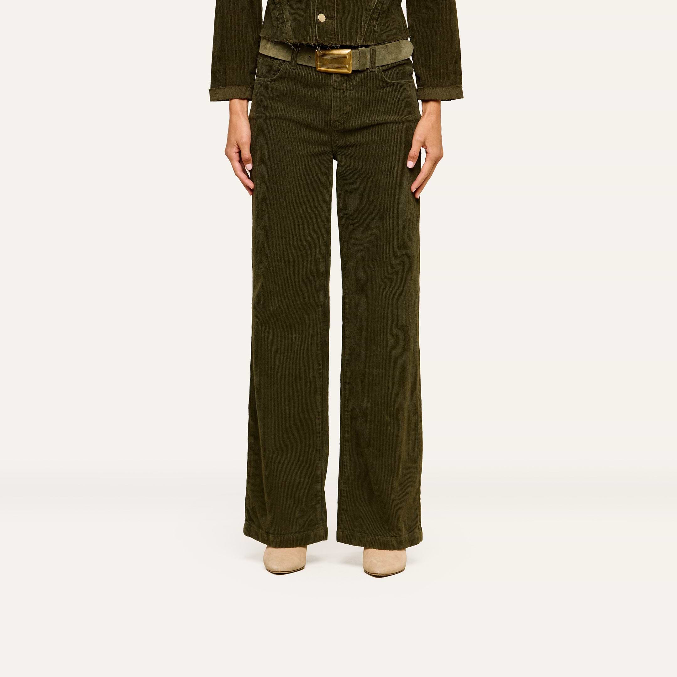 A person is standing against a plain white background, wearing the Scottie Corduroy Pant in dark green, paired with a matching jacket and beige shoes. Their head is not visible in the image.