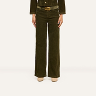 A person is standing against a plain white background, wearing the Scottie Corduroy Pant in dark green, paired with a matching jacket and beige shoes. Their head is not visible in the image.
