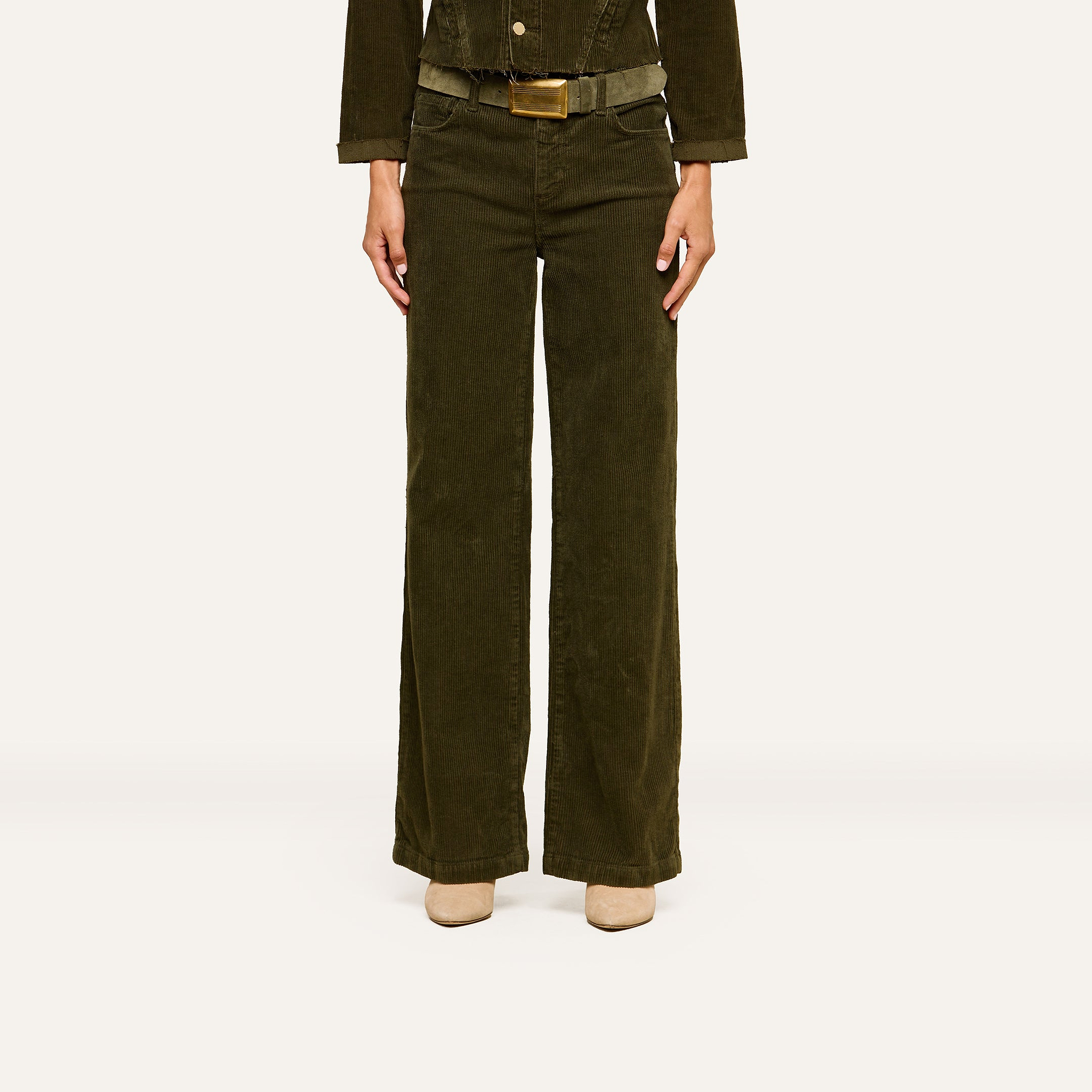 A person is standing against a plain white background, wearing the Scottie Corduroy Pant in dark green, paired with a matching jacket and beige shoes. Their head is not visible in the image.