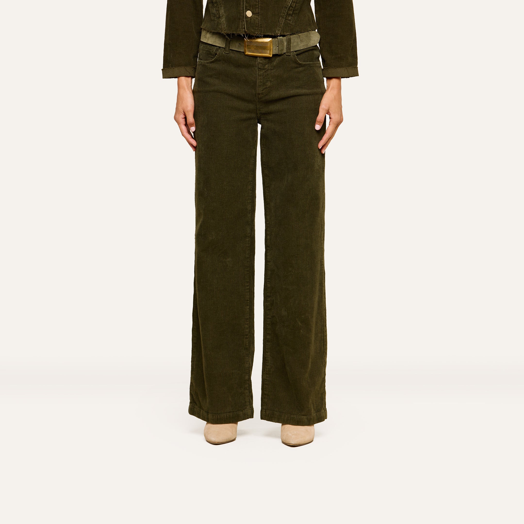 A person is standing against a plain white background, wearing the Scottie Corduroy Pant in dark green, paired with a matching jacket and beige shoes. Their head is not visible in the image.