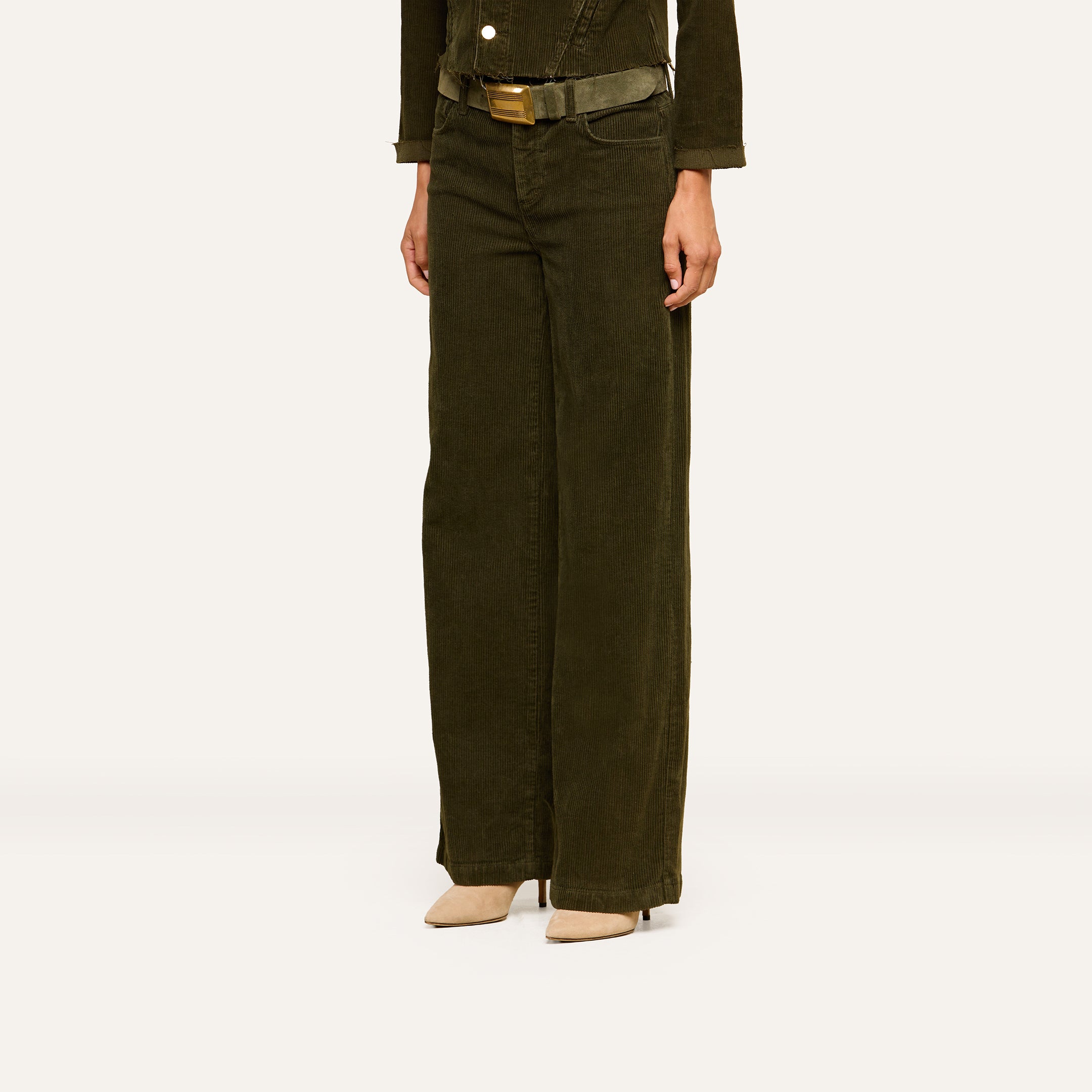 Wearing the Scottie Corduroy Pant—a high-waisted, wide-leg style in dark olive green with a matching belt—paired with beige pointed-toe heels, this look shown from shoulders down against a plain background highlights a chic fall 2026 fashion ensemble.