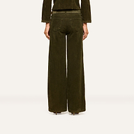A person stands facing away from the camera against a plain, light background, wearing the Scottie Corduroy Pant—high-rise, dark green wide-leg pants with two back pockets—styled for a look inspired by fall 2026 fashion and paired with a matching jacket.