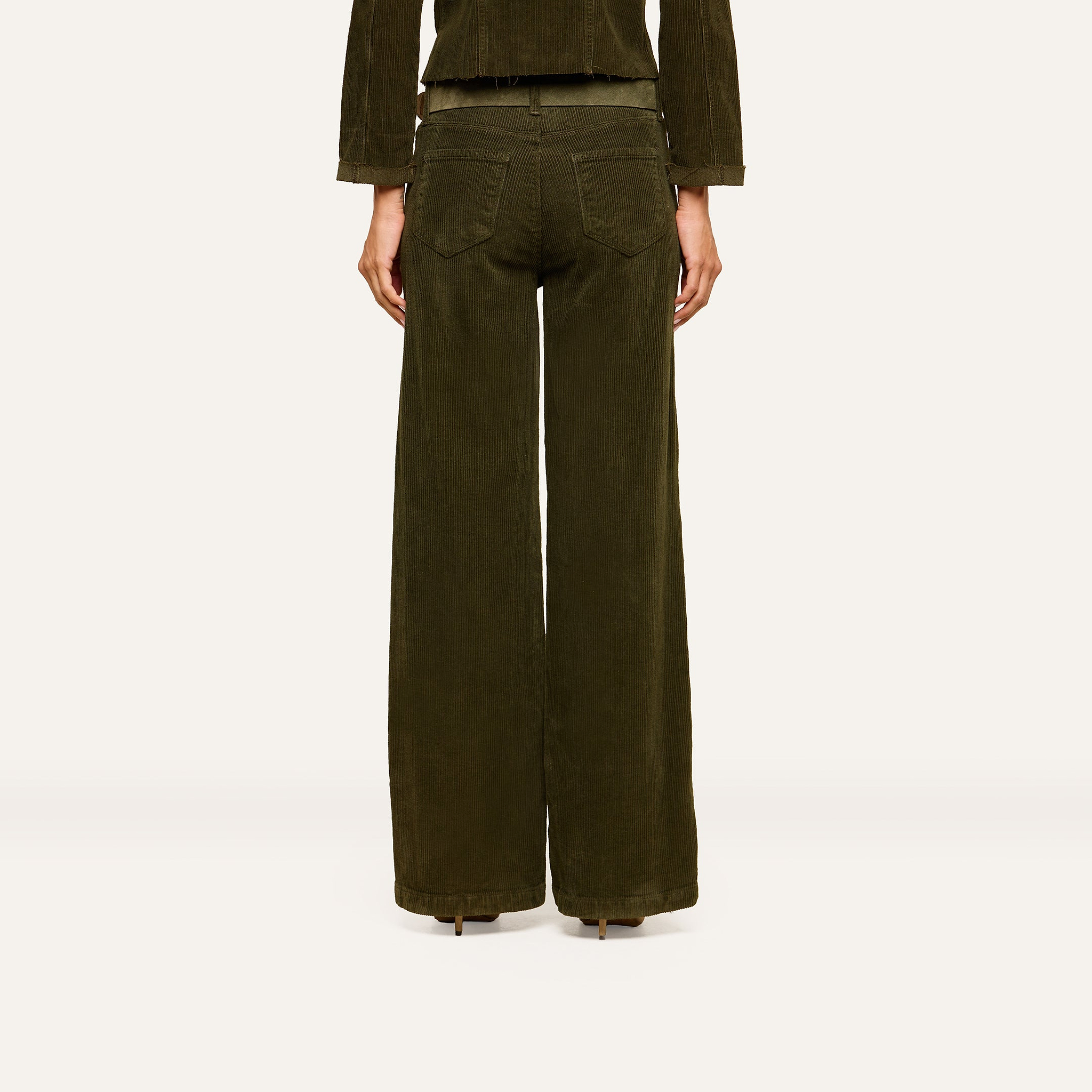 A person stands facing away from the camera against a plain, light background, wearing the Scottie Corduroy Pant—high-rise, dark green wide-leg pants with two back pockets—styled for a look inspired by fall 2026 fashion and paired with a matching jacket.
