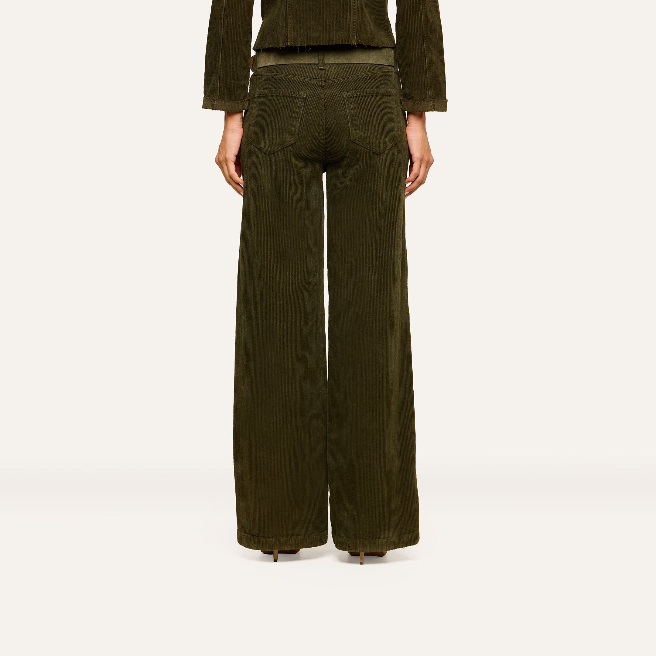 A person stands facing away from the camera against a plain, light background, wearing the Scottie Corduroy Pant—high-rise, dark green wide-leg pants with two back pockets—styled for a look inspired by fall 2026 fashion and paired with a matching jacket.