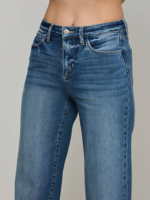 A close-up of a person wearing the Scottie Wide-Leg Jean—high-rise, blue stretch denim with a button and zip fly—shown from waist to mid-thigh against a neutral background.
