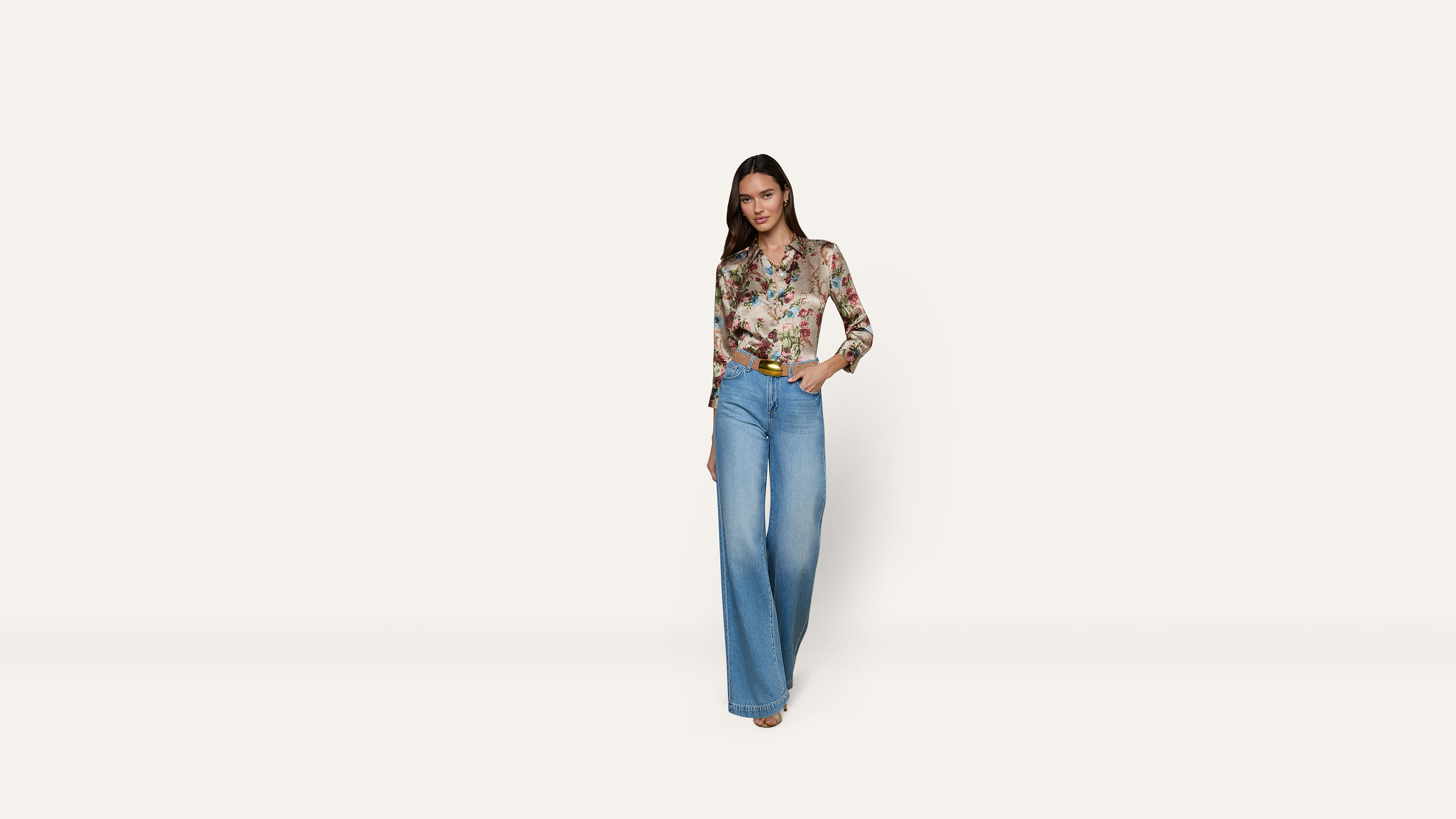 A person wearing a long-sleeved floral button-down shirt tucked into wide-leg blue jeans.