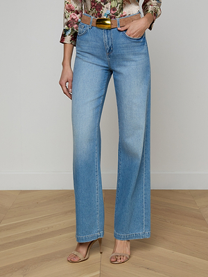 Wearing Scottie Wide-Leg Jean in light wash with a metallic gold belt, floral top, and nude heeled sandals, a person stands on a wooden floor against a plain light wall, highlighting the jeans' flattering fit.
