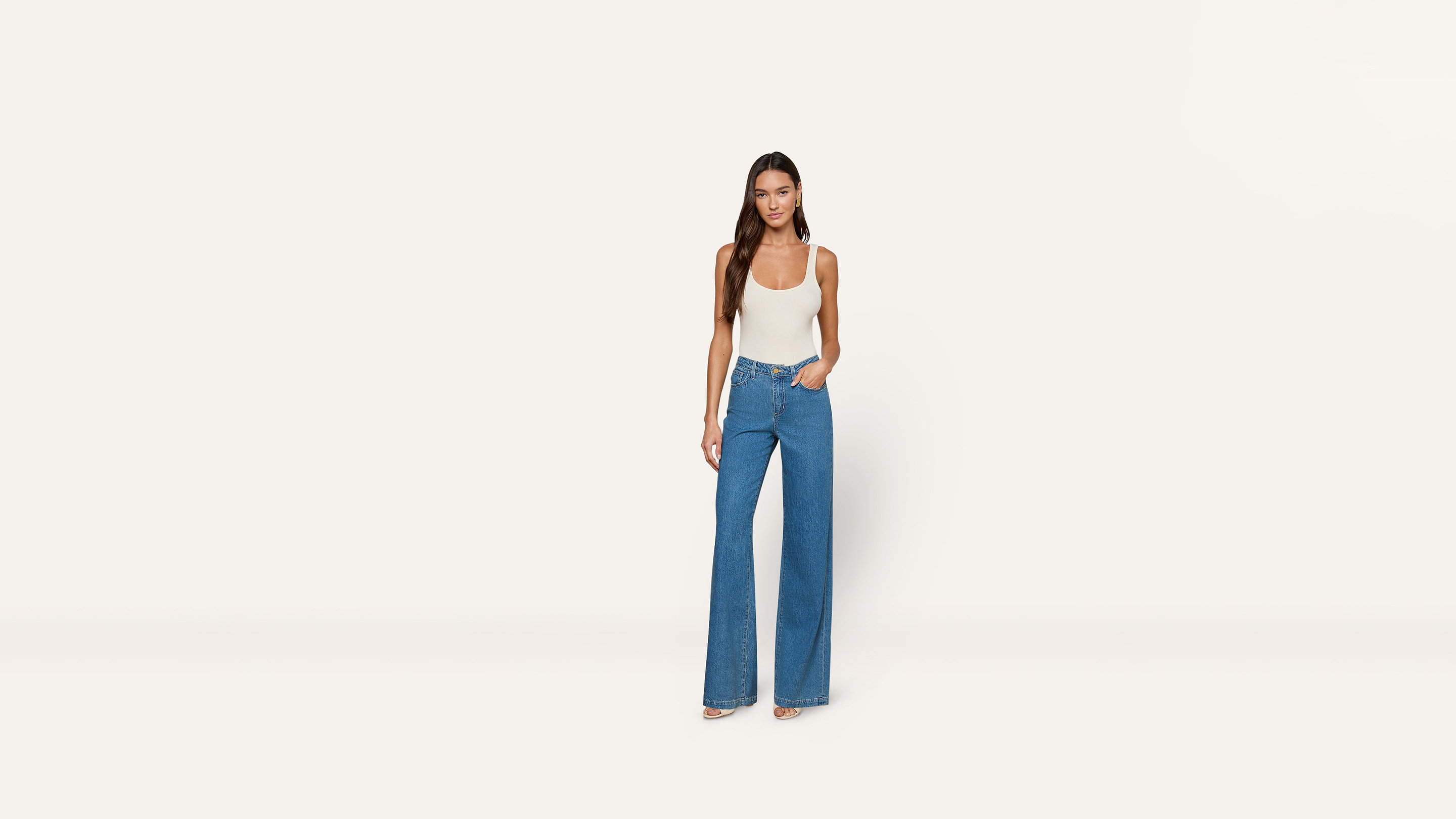 A woman wearing a cream-colored tank top and wide-leg blue jeans.