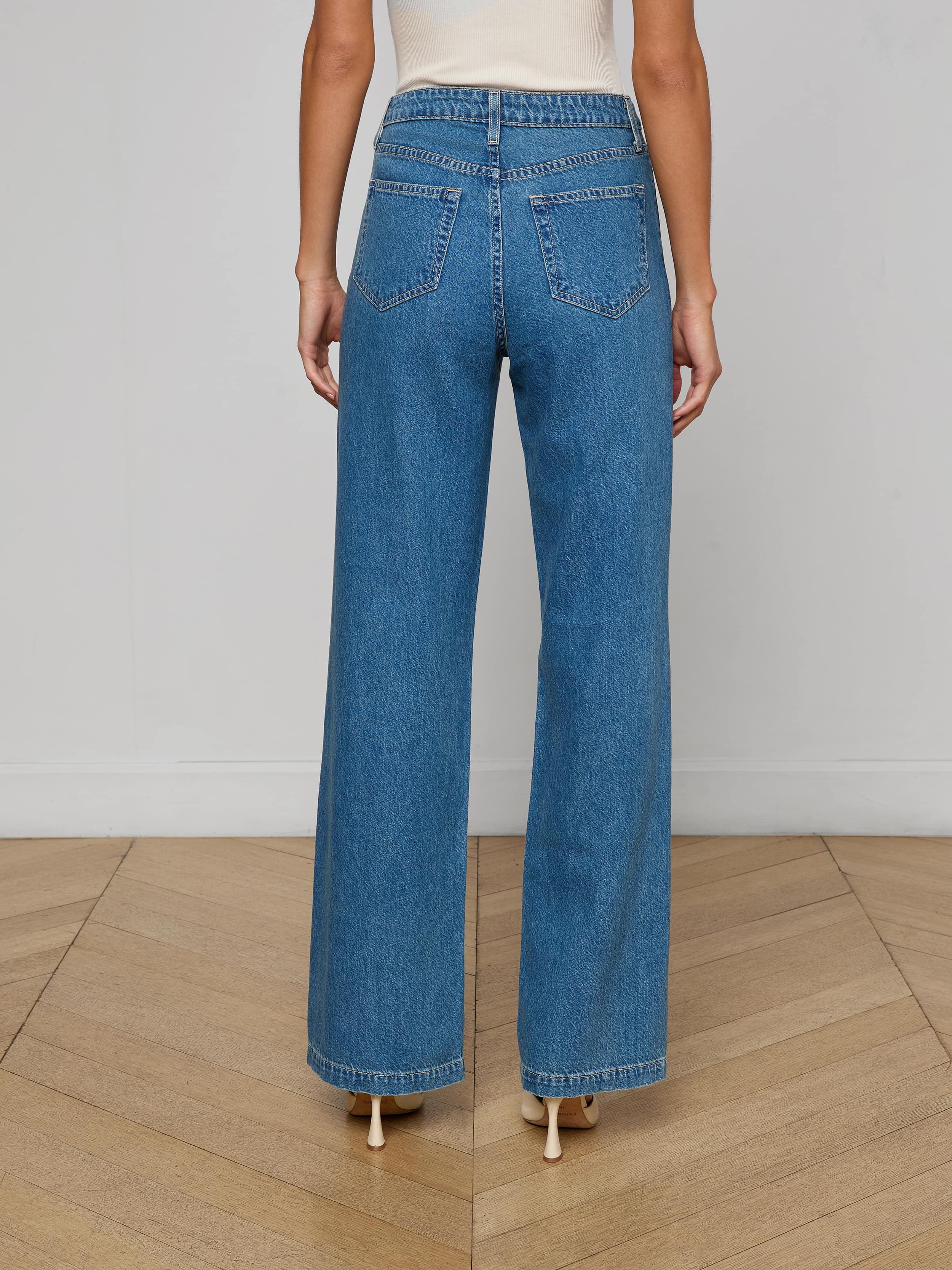 A person is shown from the back, standing against a plain white background, wearing the Scottie Wide-Leg Jean crafted from all-cotton denim in a medium wash and paired with beige heels.