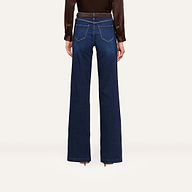 Person standing against a white background, shown from the back, wearing wide-leg dark blue jeans, a brown long-sleeve blouse, and stylish brown heeled boots.