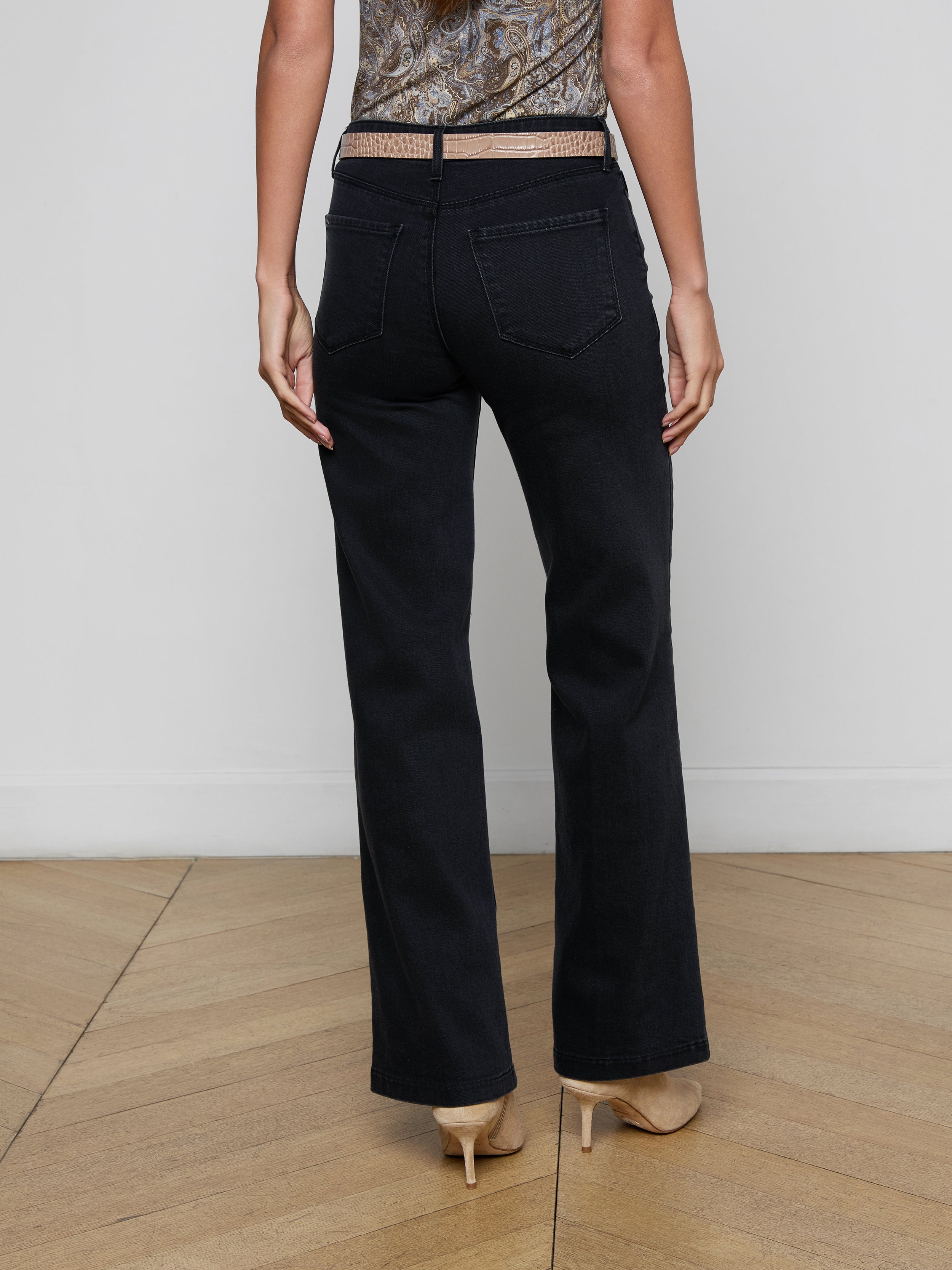 A person is shown from the back, standing against a plain light background, wearing the Scottie Wide-Leg Jean in black with a contoured waistband and beige high heels.