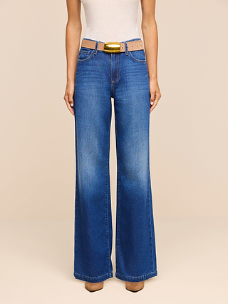 A person wearing the Scottie Wide-Leg Jean—high-rise, wide-leg blue jeans crafted from nonstretch denim—with a beige sleeveless top, a light brown belt featuring a gold buckle, and brown shoes, standing against a plain beige background.