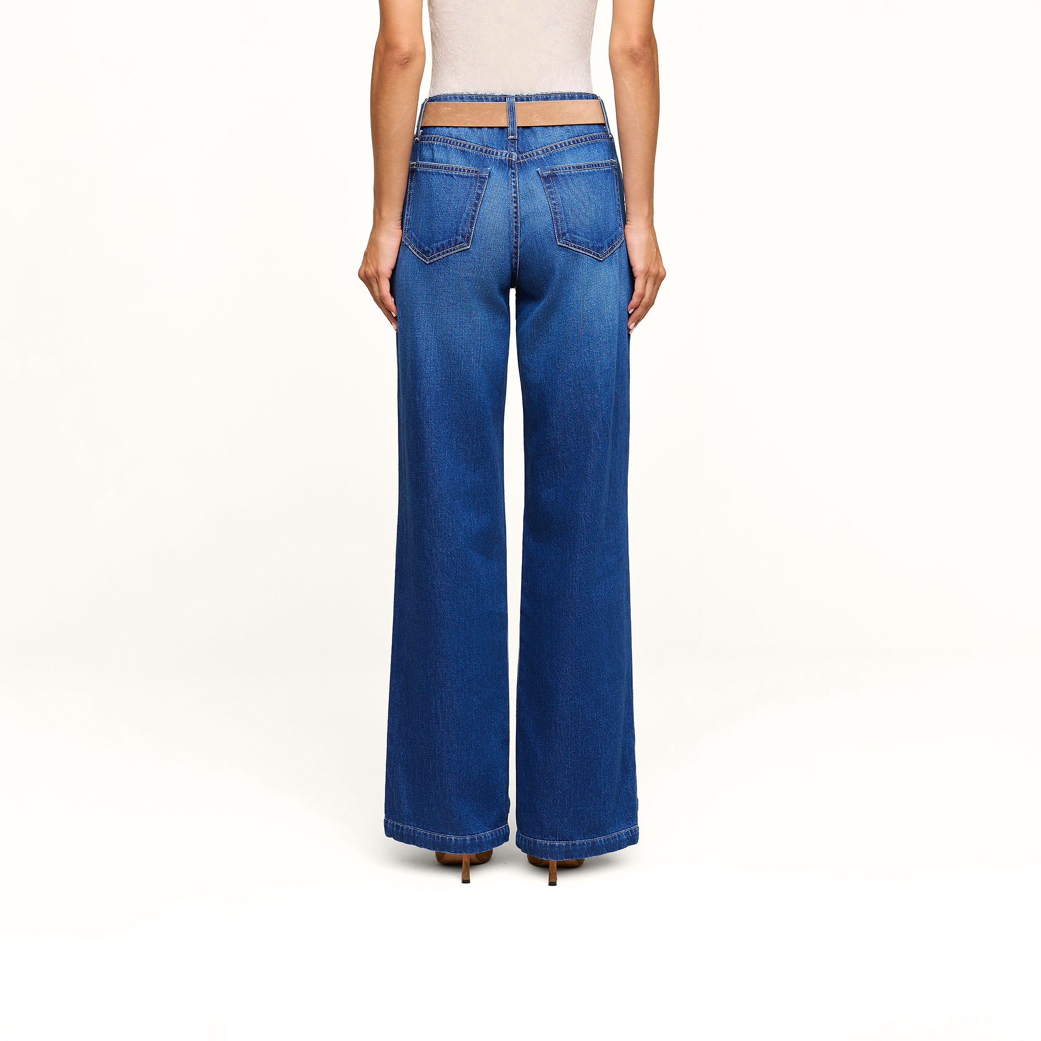 A person is shown from the back, wearing Scottie Wide-Leg Jean in an indigo wash with visible back pockets and a light-colored sleeveless top, standing against a plain white background.