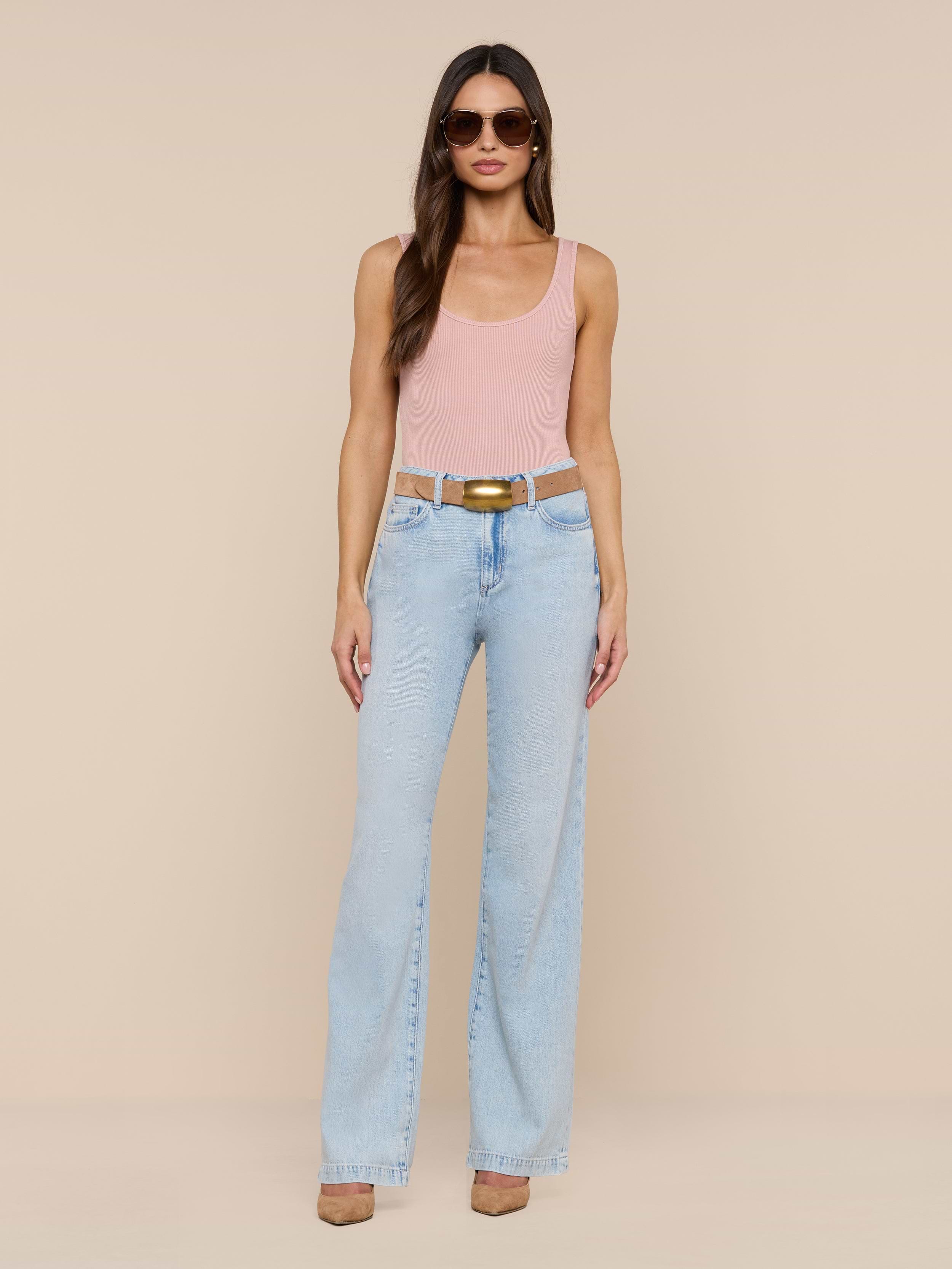 A woman stands against a plain white background wearing sunglasses, a pink tank top, brown shoes, and the Scottie Wide-Leg Jean in a light wash high-rise style with a belt.
