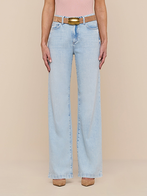 Person wearing Scottie Wide-Leg Jean in light wash, a tan belt with gold buckle, a light pink top, and tan shoes, standing against a beige background.