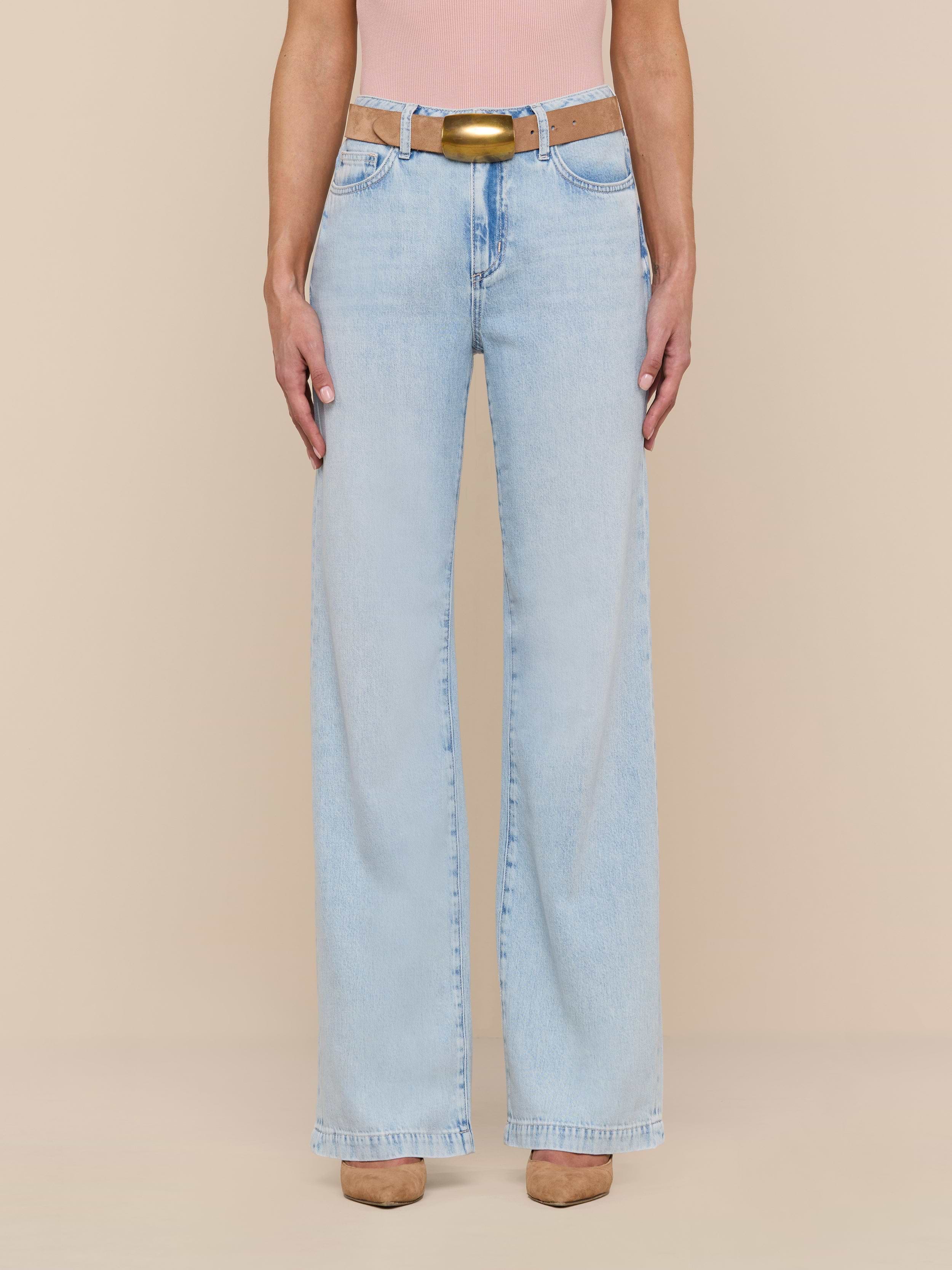 Wearing the Scottie Wide-Leg Jean in a light wash with a beige belt, a pink top, and tan shoes, the person stands against a plain white background.