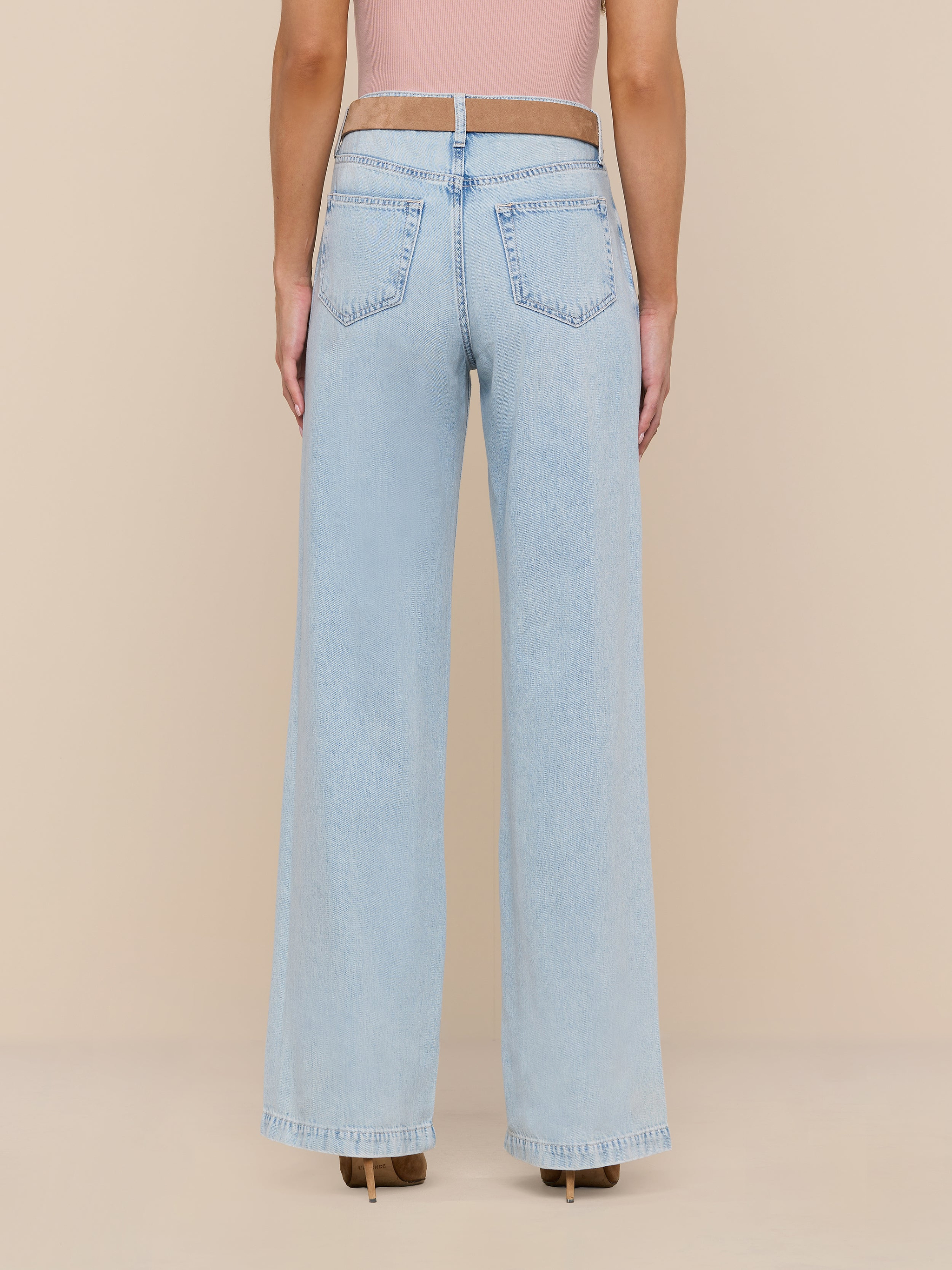 A person stands facing away against a plain white background, showcasing the back of the Scottie Wide-Leg Jean in a high-rise, light wash style, paired with a pink top.