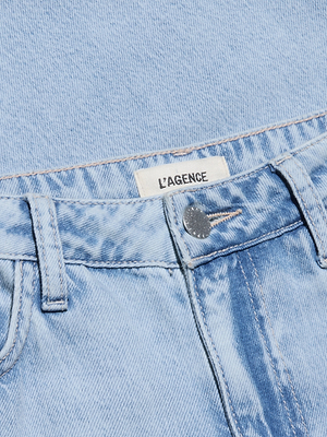 Close-up of the Scottie Wide-Leg Jean in light wash denim. Features include a high-rise fit, silver button, belt loops, and a white LAGENCE label inside the waistband. The jeans are laid flat on fabric in a matching shade.