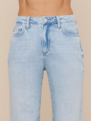 A close-up of a person wearing the Scottie Wide-Leg Jean in light wash with a high-rise fit, button and zipper closure, front pockets, and belt loops. The background is plain beige.