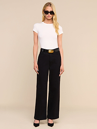 A woman with long blonde hair, wearing black sunglasses, a white short-sleeve top, and the Scottie Wide-Leg Jean paired with a black belt and black heels stands against a plain white background.