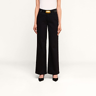 A person stands against a plain background, wearing the Scottie Wide-Leg Jean—a pair of black high-rise jeans crafted from premium stretch denim—paired with a black belt featuring a gold buckle, a white top, and black pointed-toe heels. Their arms are relaxed at their sides.