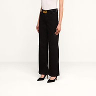 A person stands against a plain white background wearing the Scottie Wide-Leg Jean in black high-rise premium stretch denim, paired with a white sleeveless top, black high heels, and a black belt with a gold buckle.