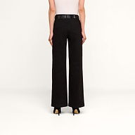 A person stands facing away on a plain white background, wearing a white sleeveless top, the Scottie Wide-Leg Jean in black high-rise, a black belt, and black heels.