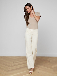 A woman wears a beige v-neck t-shirt tucked into off-white Scottie Wide-Leg Jean pants, styled with a tan belt featuring a large gold buckle.
