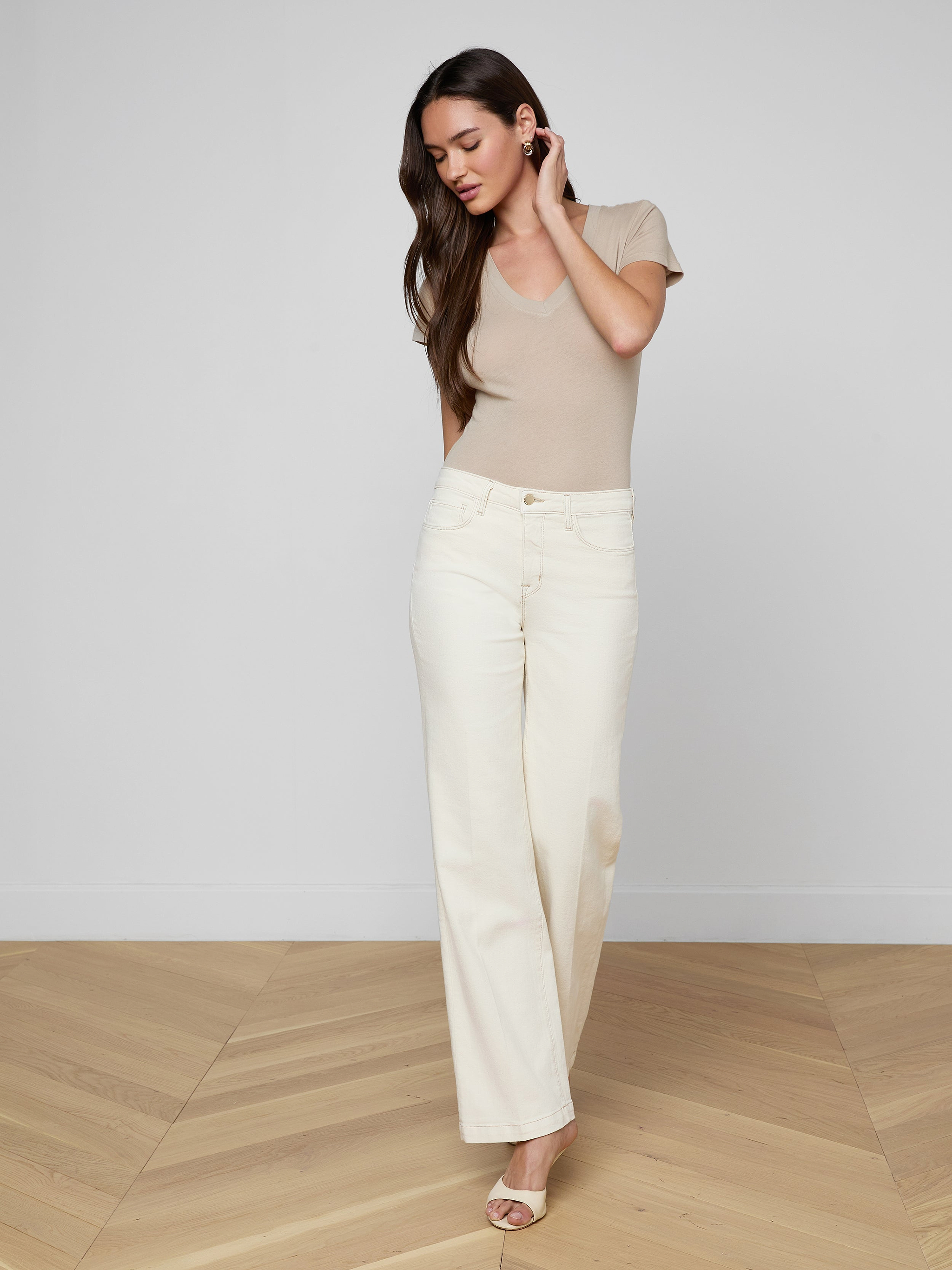 A woman wears a beige v-neck t-shirt tucked into off-white Scottie Wide-Leg Jean pants, styled with a tan belt featuring a large gold buckle.