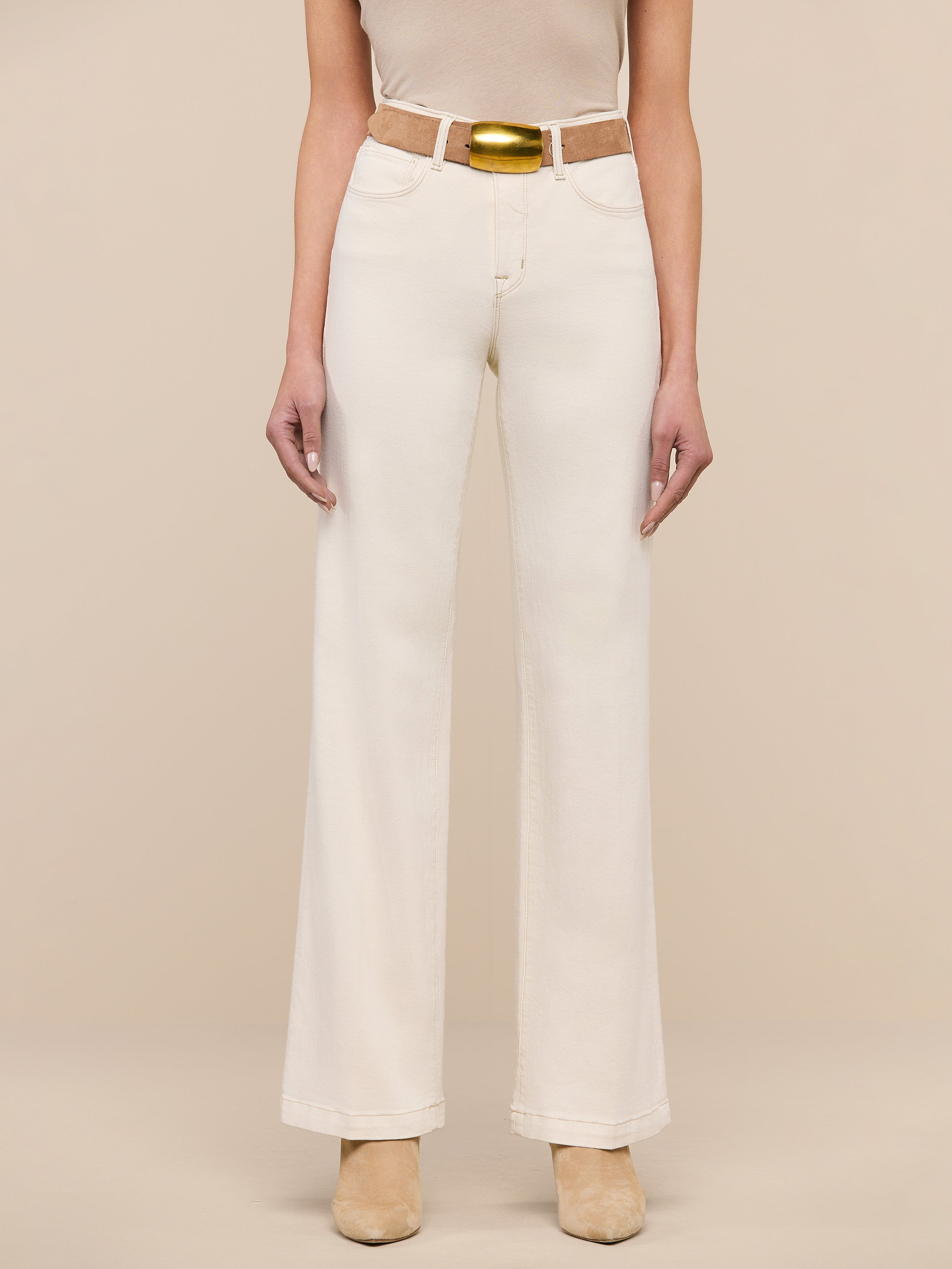 A person wearing the Scottie Wide-Leg Jean in an off-white wash, styled with a tan belt and beige shoes, stands against a plain white background. The upper body is mostly out of frame.