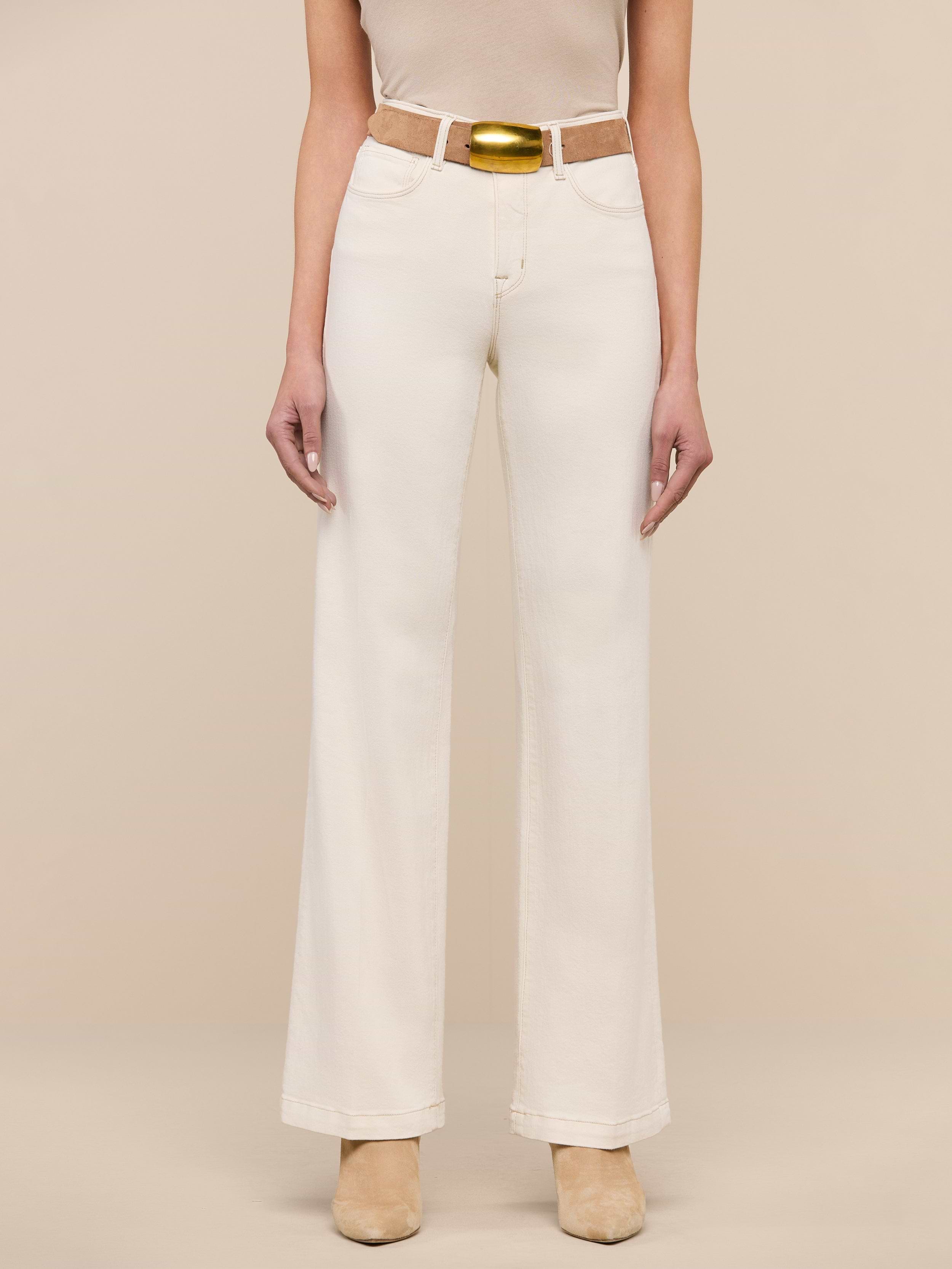 A person wearing the Scottie Wide-Leg Jean in an off-white wash, styled with a tan belt and beige shoes, stands against a plain white background. The upper body is mostly out of frame.