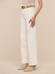 A person wearing the Scottie Wide-Leg Jean in cream, styled with a brown belt and beige heeled shoes, stands against a plain white background.
