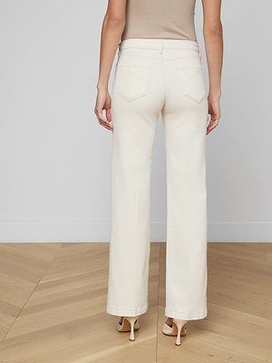 A person stands on a wooden floor facing away, wearing a beige sleeveless top, beige heels, and Scottie Wide-Leg Jean featuring an off-white high-rise waistband.